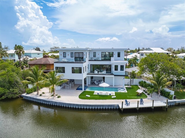 back of property with a water view, a balcony, a patio area, and a lawn