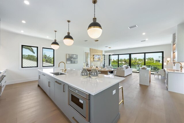 kitchen featuring light wood-type flooring, pendant lighting, an island with sink, sink, and white cabinets