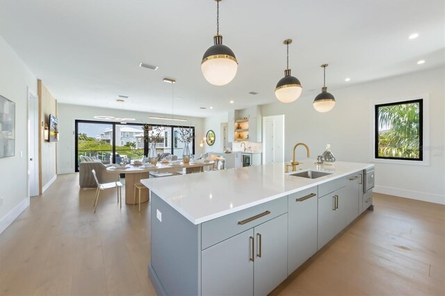 kitchen with light wood-type flooring, gray cabinets, a kitchen island with sink, and sink