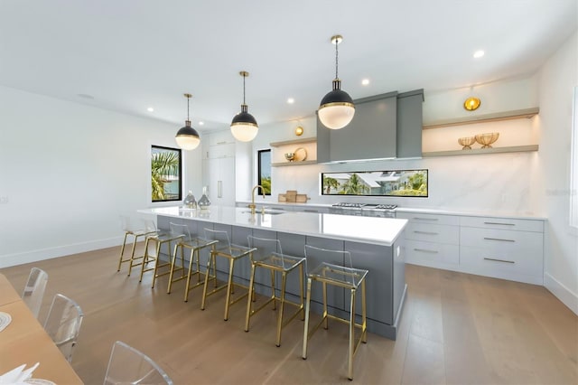 kitchen featuring hanging light fixtures, light wood-type flooring, a large island with sink, sink, and a breakfast bar