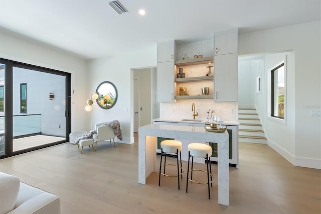 kitchen with light wood-type flooring, a breakfast bar area, backsplash, and sink