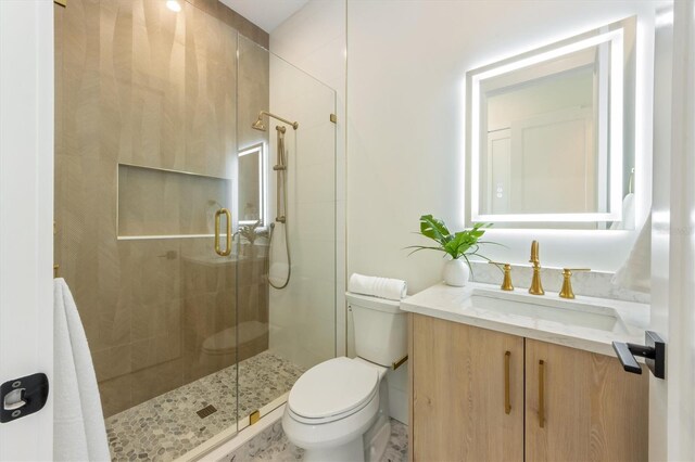 bathroom featuring a shower with door, vanity, and toilet