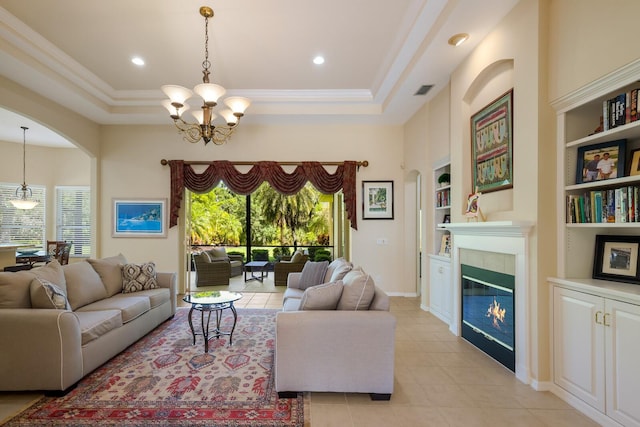 tiled living room with a notable chandelier, built in features, a tray ceiling, and a tiled fireplace