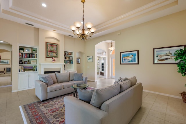 tiled living room with a raised ceiling, a notable chandelier, and built in shelves