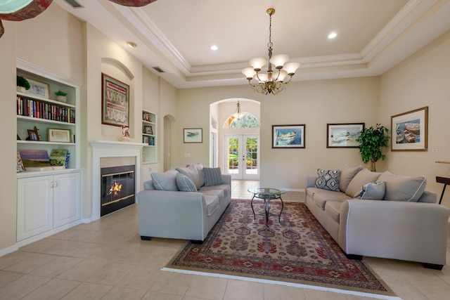 living room with a notable chandelier, light tile flooring, a raised ceiling, a tiled fireplace, and built in features