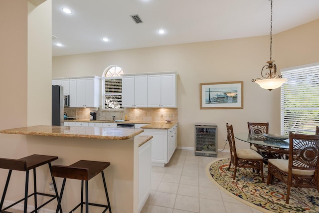 kitchen featuring backsplash, beverage cooler, decorative light fixtures, and white cabinetry