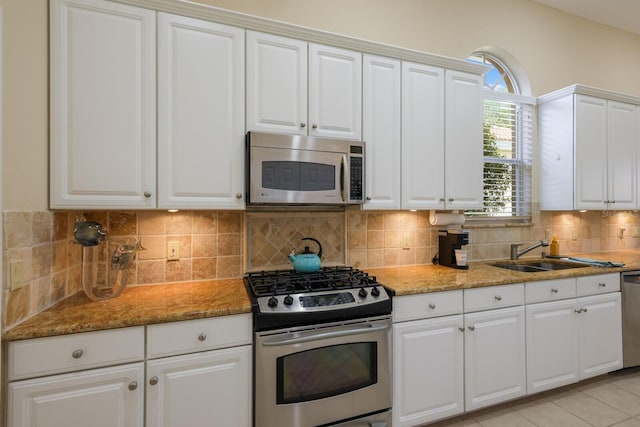 kitchen with appliances with stainless steel finishes, light tile floors, white cabinets, sink, and backsplash