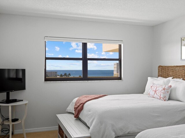 bedroom featuring multiple windows, a water view, carpet floors, and a textured ceiling