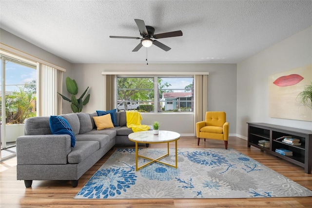 living room with a textured ceiling, ceiling fan, and light hardwood / wood-style flooring