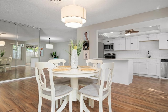 dining space with ceiling fan, sink, a tray ceiling, and hardwood / wood-style floors