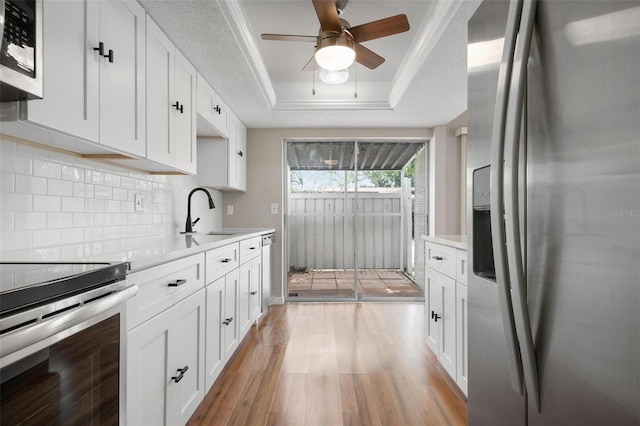 kitchen with stainless steel appliances, light hardwood / wood-style flooring, white cabinetry, backsplash, and a raised ceiling