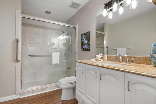 bathroom featuring toilet, a shower with shower door, hardwood / wood-style flooring, a textured ceiling, and vanity