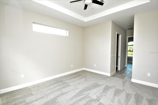 carpeted empty room with ceiling fan and a raised ceiling