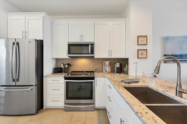 kitchen with sink, appliances with stainless steel finishes, white cabinetry, light stone counters, and tasteful backsplash