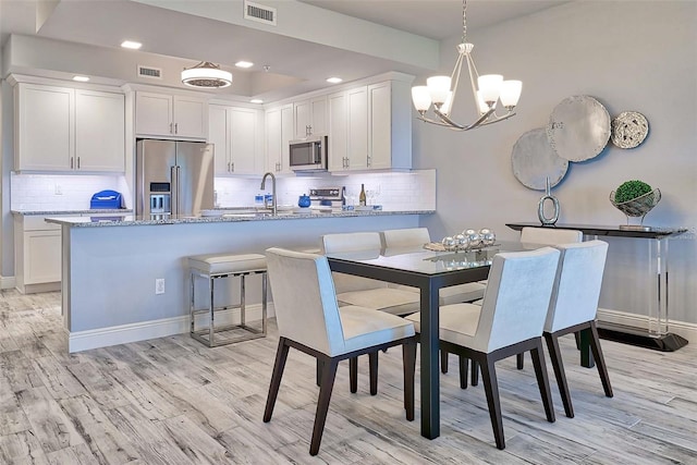 dining area with light wood-type flooring, sink, and an inviting chandelier