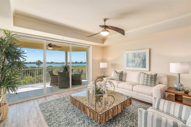 living room featuring a raised ceiling, a water view, wood-type flooring, and ornamental molding