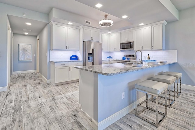 kitchen featuring light stone countertops, a kitchen breakfast bar, kitchen peninsula, white cabinets, and appliances with stainless steel finishes