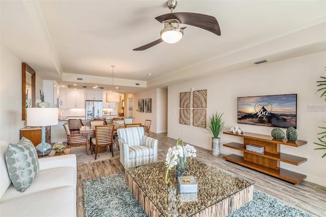 living room with a tray ceiling, ceiling fan, and light hardwood / wood-style floors