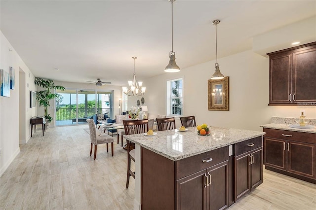 kitchen featuring pendant lighting, a breakfast bar, ceiling fan with notable chandelier, light wood-type flooring, and a kitchen island