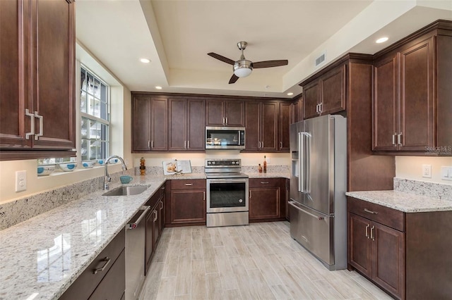 kitchen featuring appliances with stainless steel finishes, light stone counters, dark brown cabinets, ceiling fan, and sink