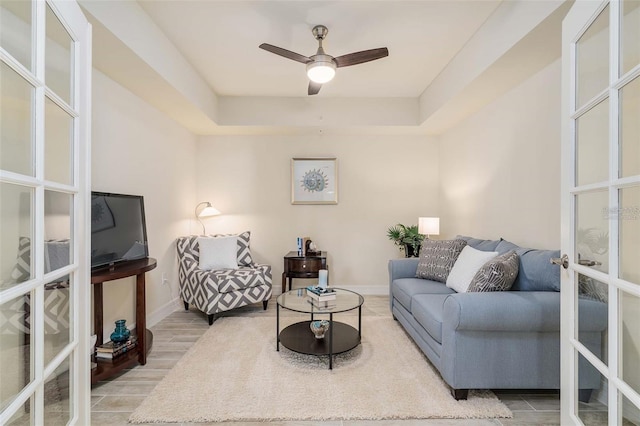 living room featuring a tray ceiling, ceiling fan, and french doors