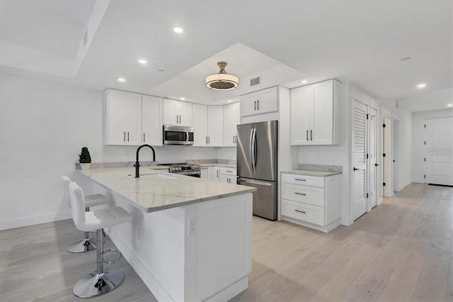 kitchen featuring stainless steel appliances, white cabinetry, a sink, light stone countertops, and a peninsula