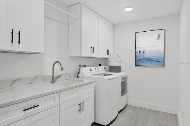 laundry area featuring cabinet space, baseboards, light wood-type flooring, washing machine and dryer, and a sink