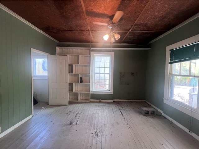 unfurnished room featuring wood-type flooring, wooden walls, ceiling fan, and crown molding