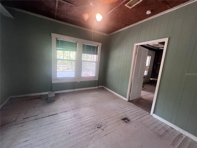 spare room featuring wooden walls, light hardwood / wood-style flooring, and crown molding