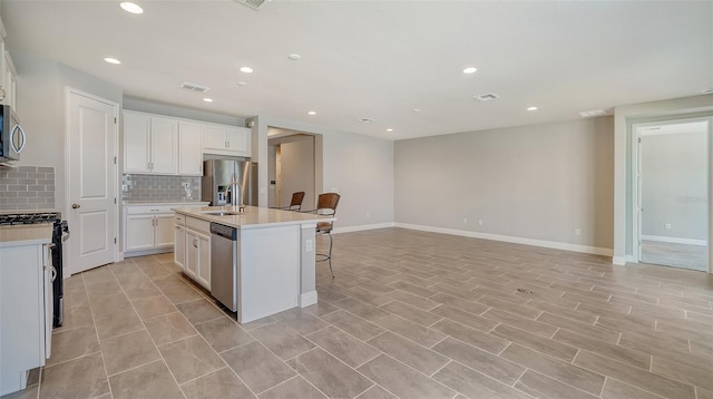 kitchen with a kitchen bar, a kitchen island with sink, decorative backsplash, white cabinets, and stainless steel appliances