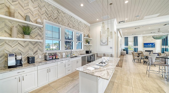 kitchen with a center island, crown molding, light stone countertops, white cabinetry, and hanging light fixtures