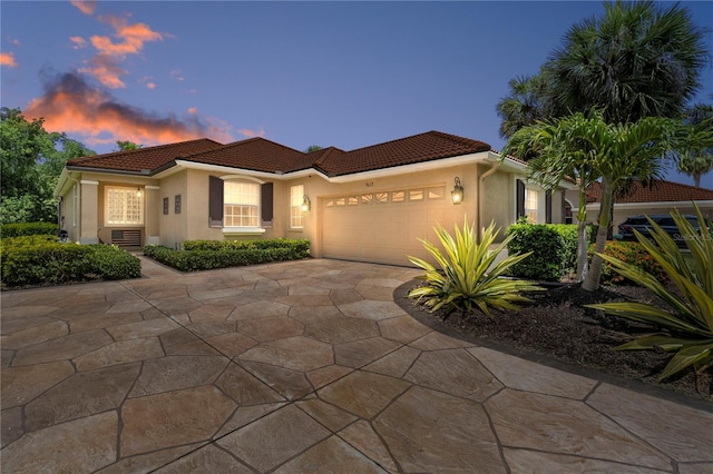 mediterranean / spanish-style house featuring a tiled roof, concrete driveway, an attached garage, and stucco siding