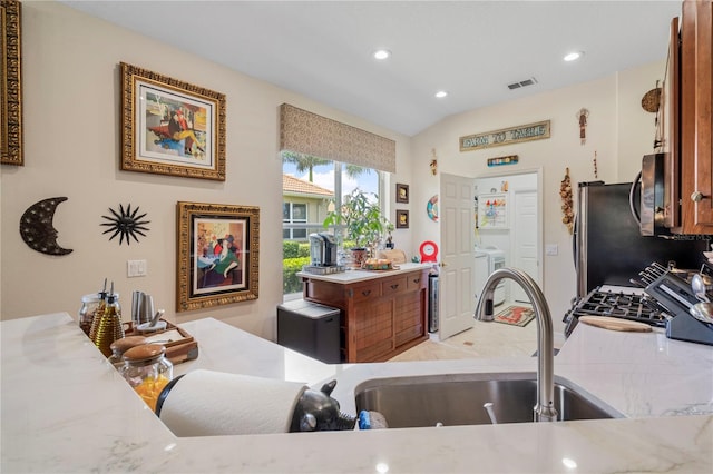 kitchen featuring lofted ceiling, washer / dryer, light stone countertops, and stainless steel appliances