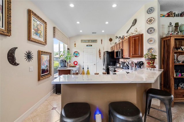 kitchen with range, kitchen peninsula, fridge, light tile patterned floors, and a kitchen breakfast bar