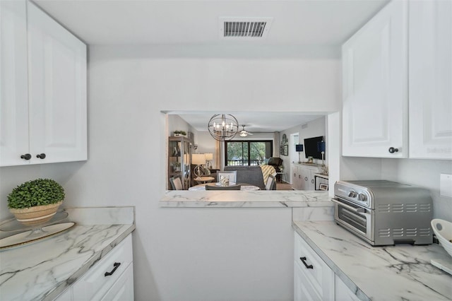 kitchen with a chandelier, white cabinetry, and light stone countertops