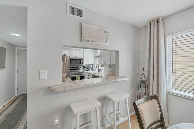 kitchen with white cabinetry, kitchen peninsula, appliances with stainless steel finishes, a breakfast bar area, and light hardwood / wood-style floors