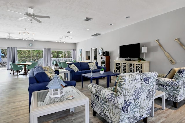 living room with light hardwood / wood-style flooring, ceiling fan, rail lighting, and a textured ceiling