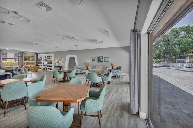 dining room with rail lighting, light hardwood / wood-style flooring, ceiling fan, and a textured ceiling