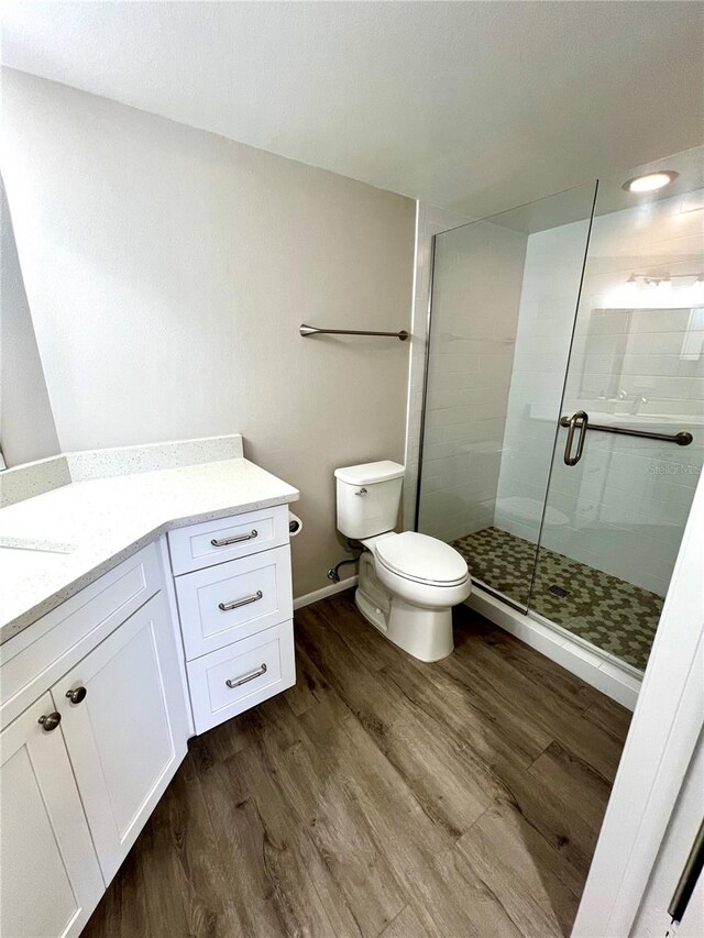 bathroom featuring wood-type flooring, vanity, toilet, and a shower with door