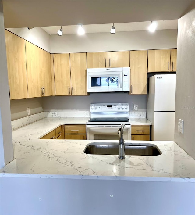 kitchen with light stone countertops, sink, kitchen peninsula, white appliances, and light brown cabinetry