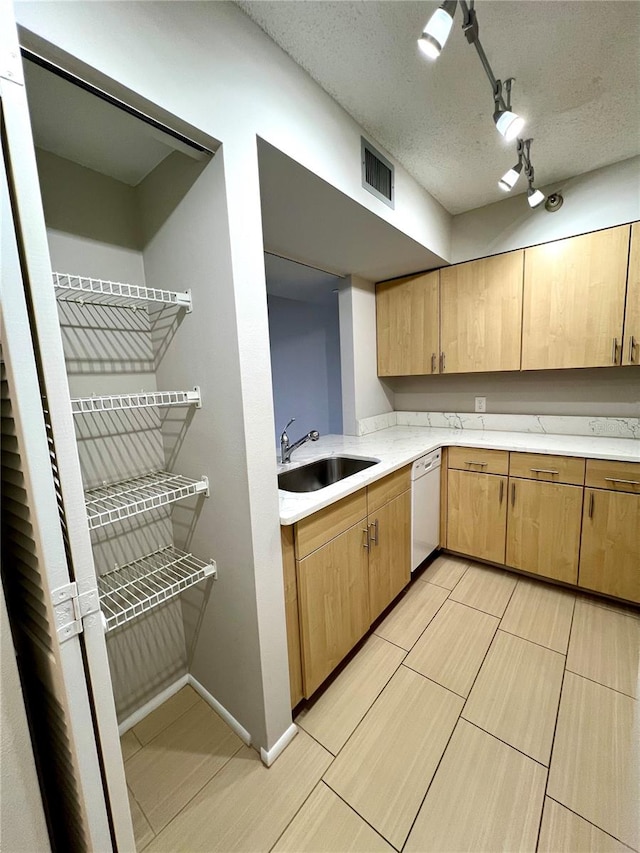 kitchen with white dishwasher, a textured ceiling, sink, and track lighting