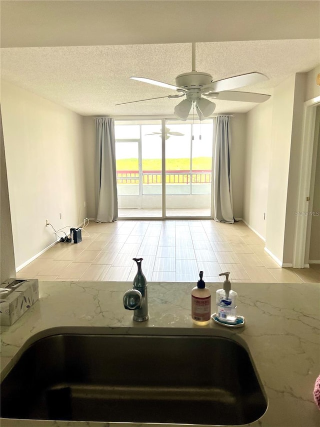 interior space featuring ceiling fan, sink, a wall of windows, a textured ceiling, and light tile patterned flooring