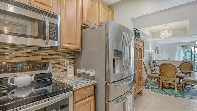 kitchen with stainless steel appliances, tasteful backsplash, a raised ceiling, an inviting chandelier, and light tile floors