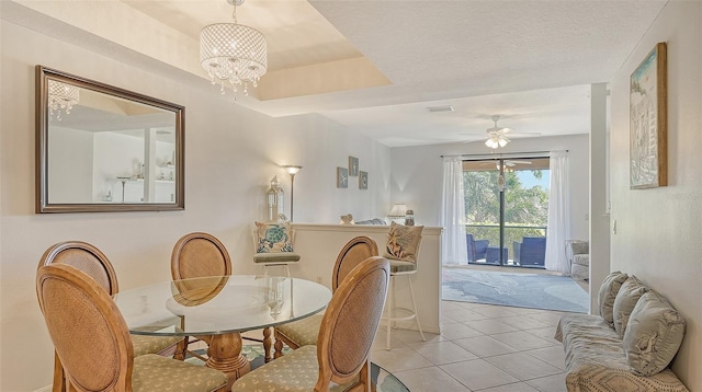 tiled dining space featuring ceiling fan with notable chandelier, a textured ceiling, and a tray ceiling