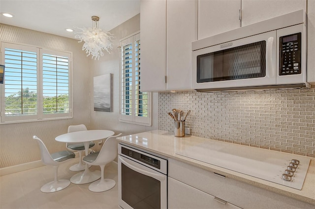 kitchen with appliances with stainless steel finishes, a healthy amount of sunlight, white cabinetry, and an inviting chandelier