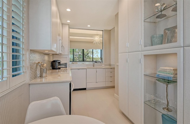 kitchen with white cabinets, backsplash, white dishwasher, light tile floors, and sink