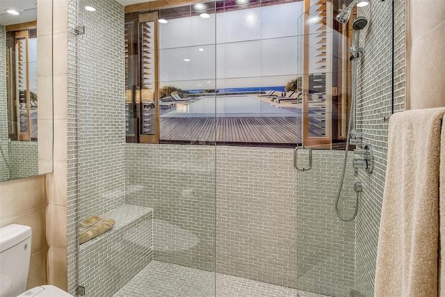 bathroom with tile walls, toilet, and a shower with shower door