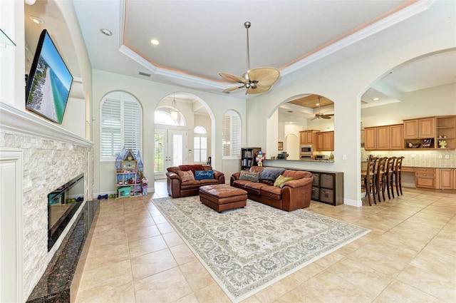 tiled living room with ceiling fan, a fireplace, a raised ceiling, ornamental molding, and french doors