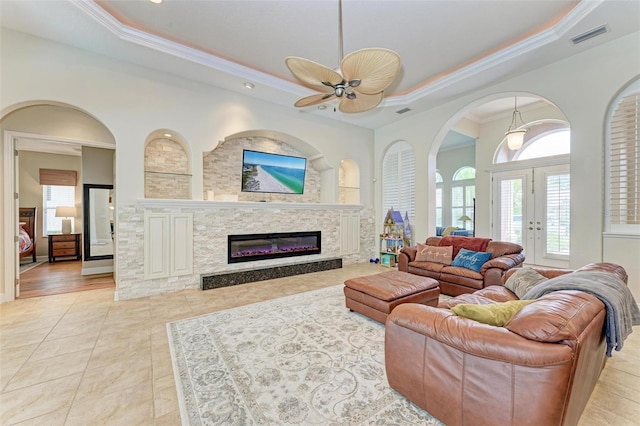 tiled living room featuring ceiling fan, crown molding, a raised ceiling, and a fireplace