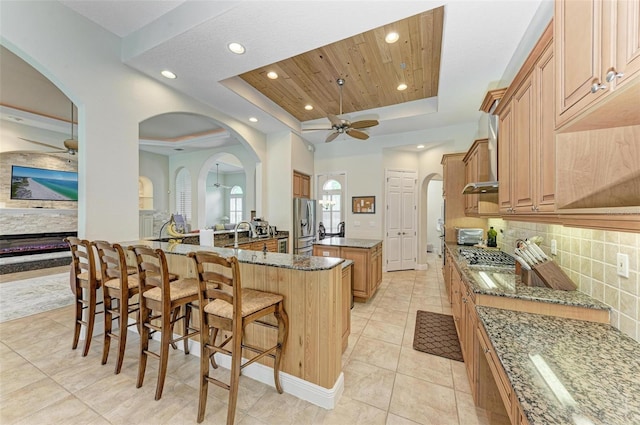 kitchen featuring a breakfast bar, a kitchen island with sink, dark stone counters, and a tray ceiling